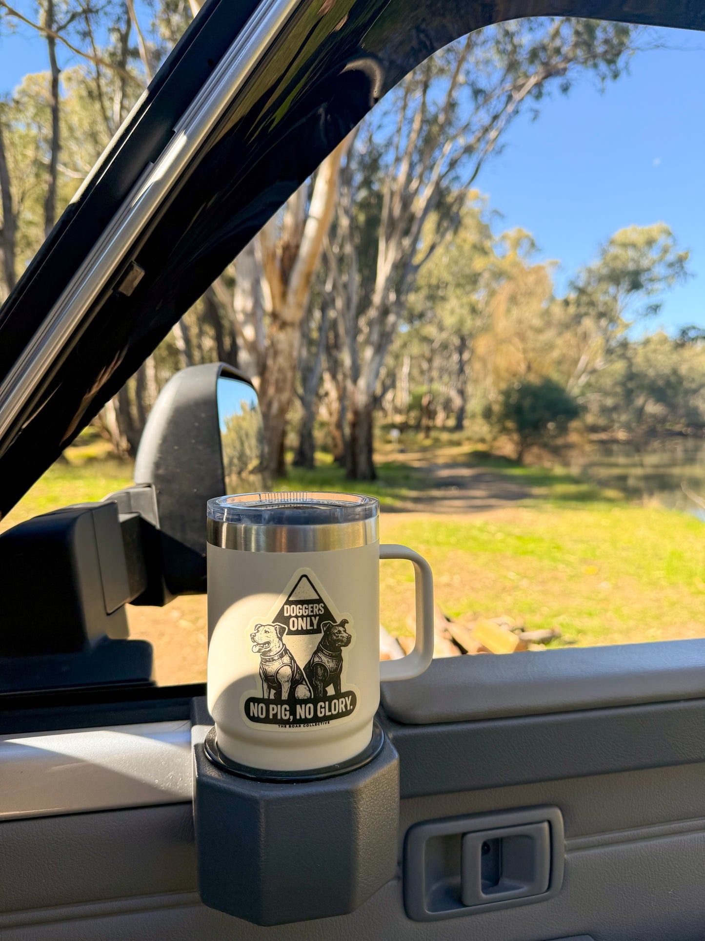 No Pig No Glory sticker placed on a drink holder inside a 4WD vehicle, set against a scenic Australian bush backdrop.