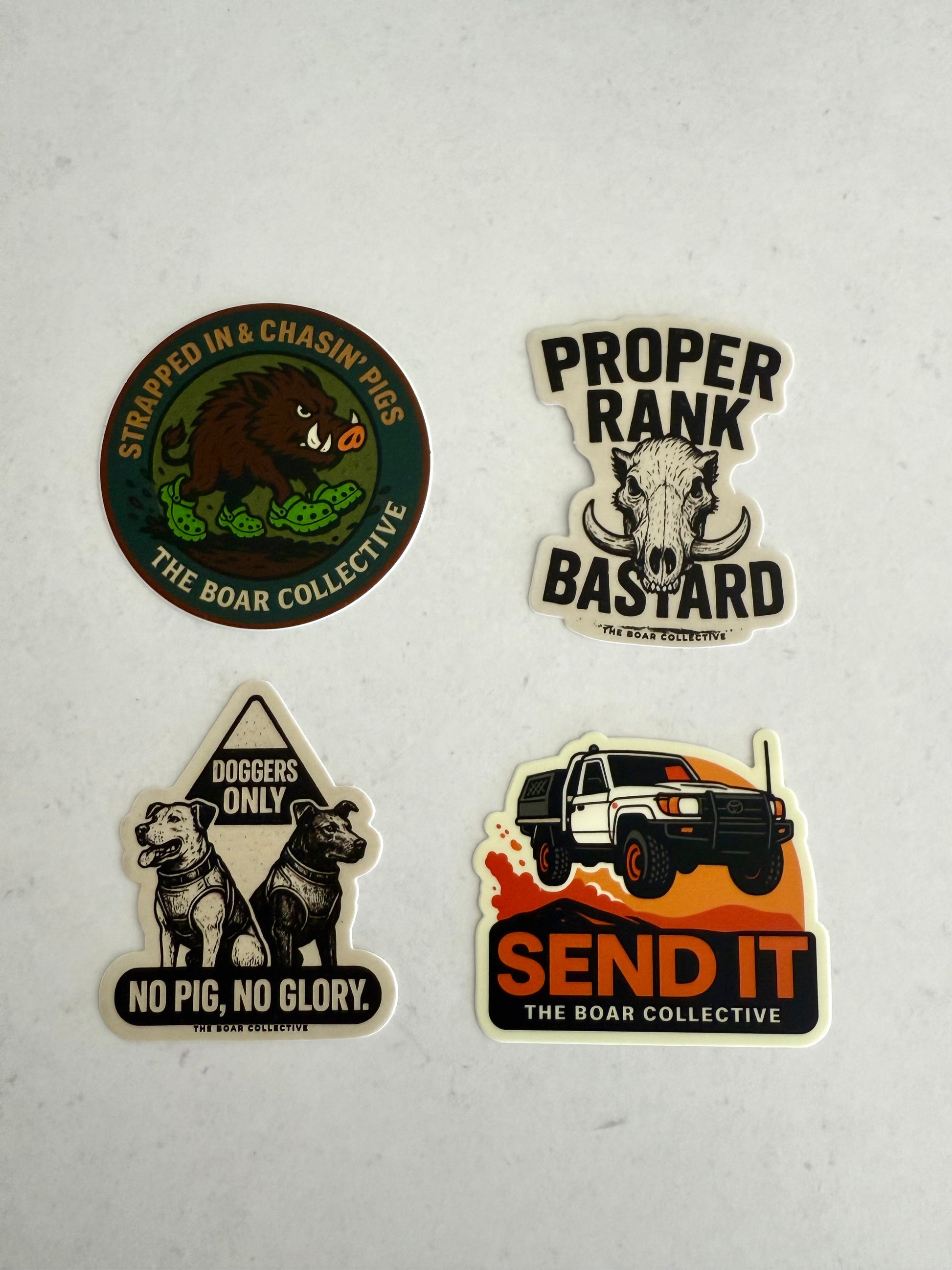 The Boar Collective sticker pack featuring four hunting-themed designs: Send It 4WD, Proper Rank Bastard, Strapped In & Chasin’ Pigs, and No Pig No Glory with pig dogs