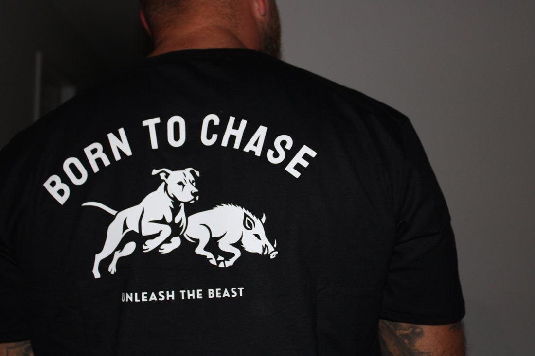 Man wearing black “Born to Chase” hunting t-shirt featuring a pig dog chasing a wild boar with the slogan “Unleash the Beast” on the back. Hunting lifestyle apparel from Australia.
