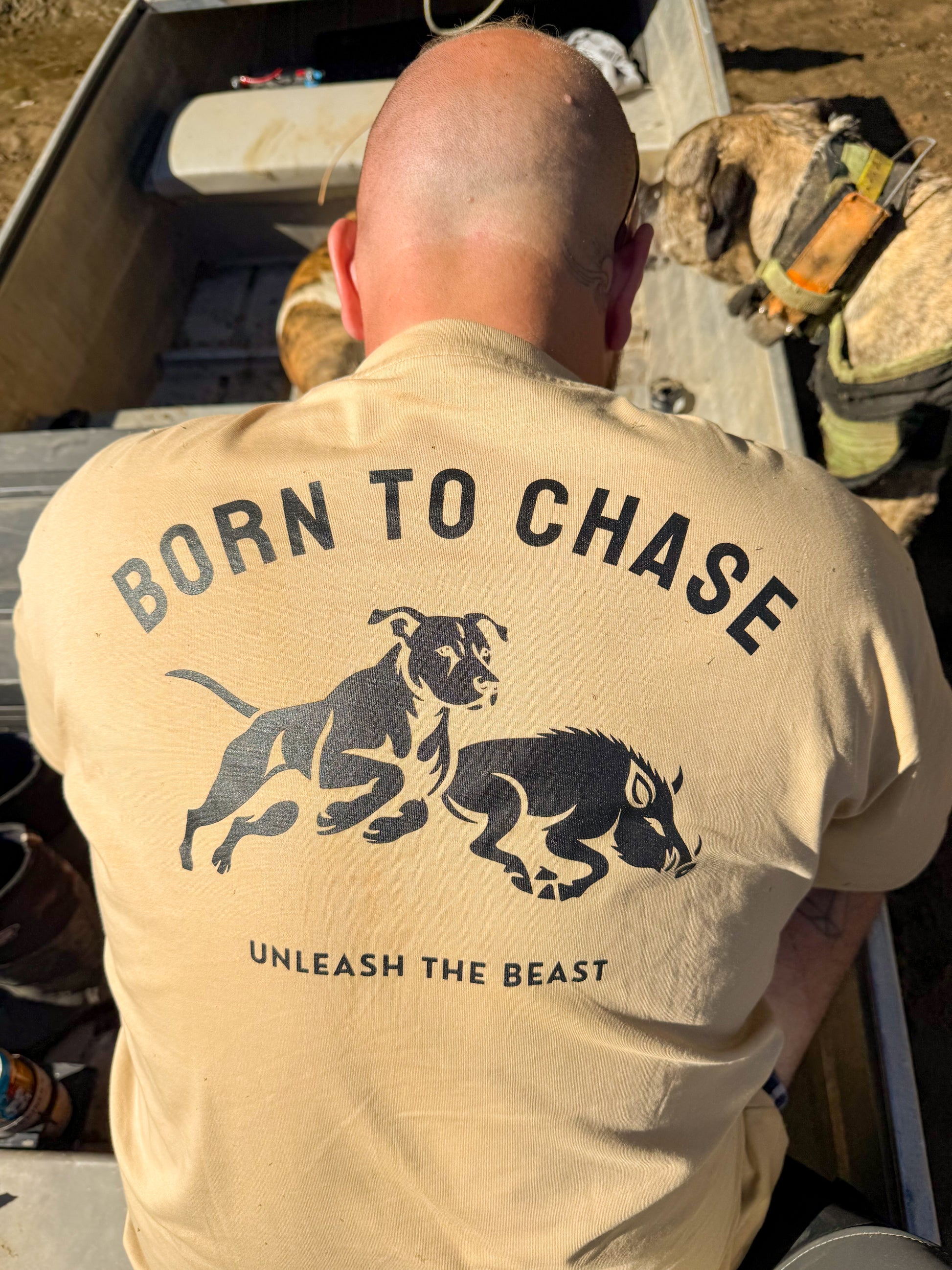 Close-up of the tan Born to Chase T-shirt from The Boar Collective clearly displaying the back print design, worn outdoors on a hunting trip.